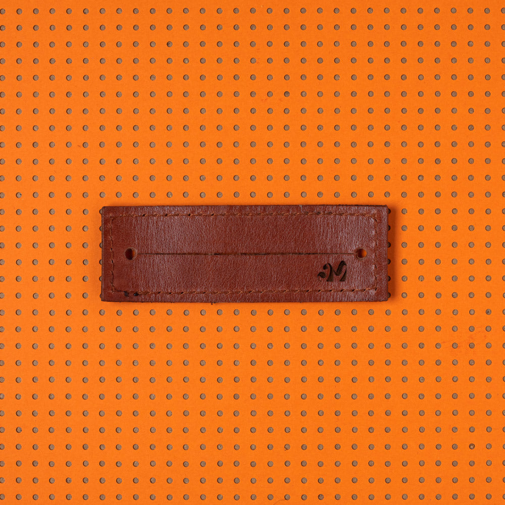 productfoto 2-strap haarband kleur Sienna bruin, plat, binnenzijde product met logo AM in leer gestanst. Achtergrond van het beeld is oranje met bruine stippen