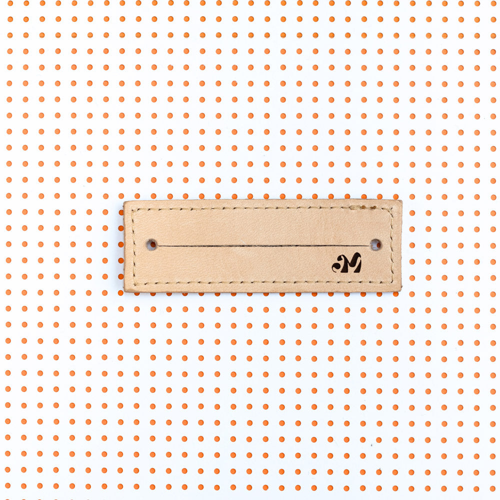 productfoto. 2-strap cover in kleur cognac plat, binnenzijde product met logo AM rechtsonder. Achtergrond van het beeld is wit met oranje stippen witte