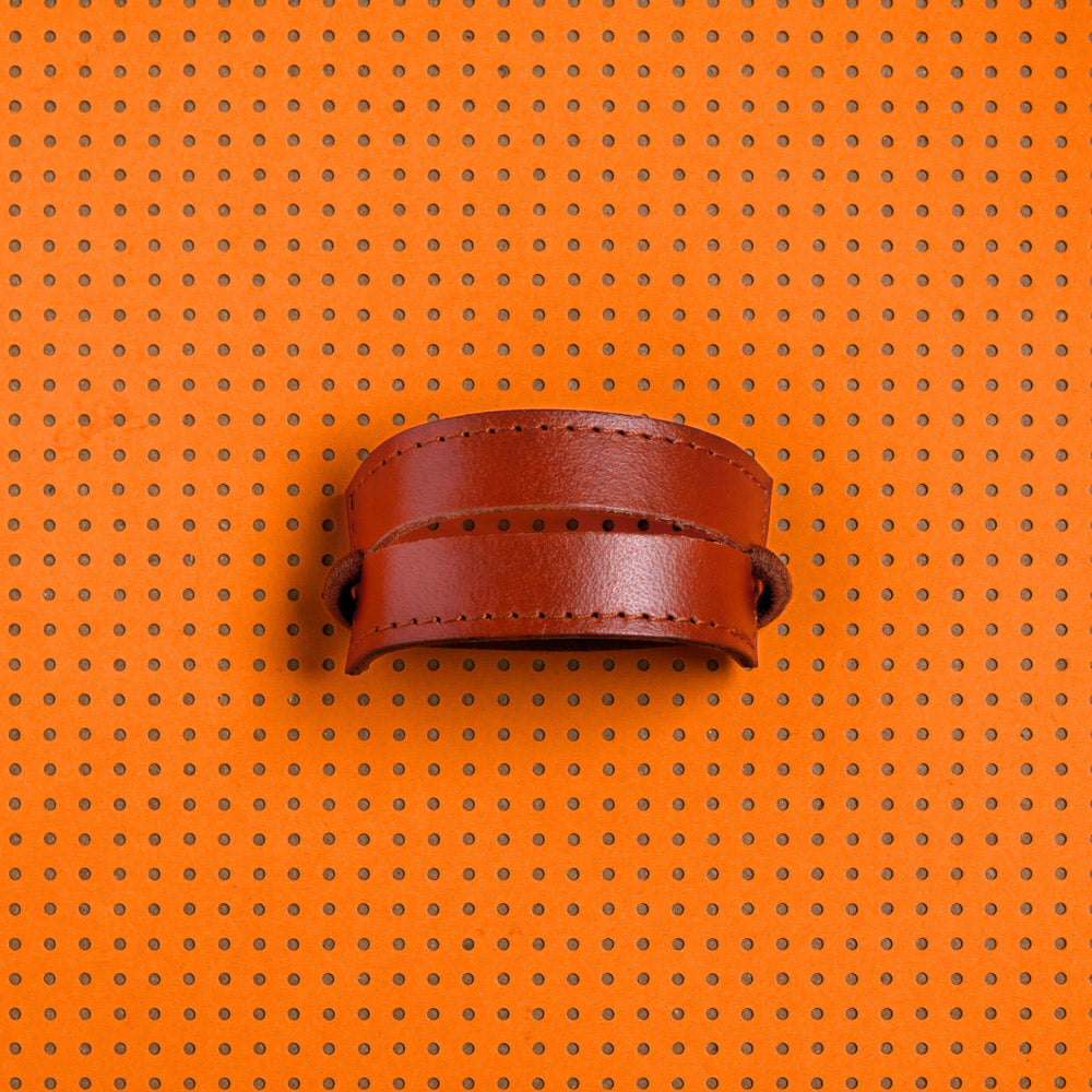 productfoto. 2-strap cover in kleur sienna bruin met elastiek erdoor. Achtergrond van het beeld is oranje met bruine stippen 