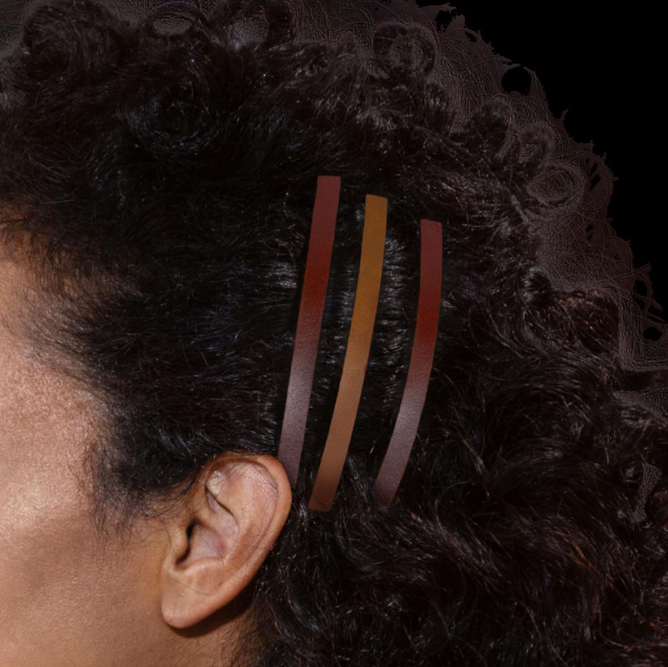 Close up van zijkant hoofd model, met dik donker krullend haar. Haar is vastgezet aan de zijkant met 3 dunne leren haarclips in kleur Sienna bruin en cognac