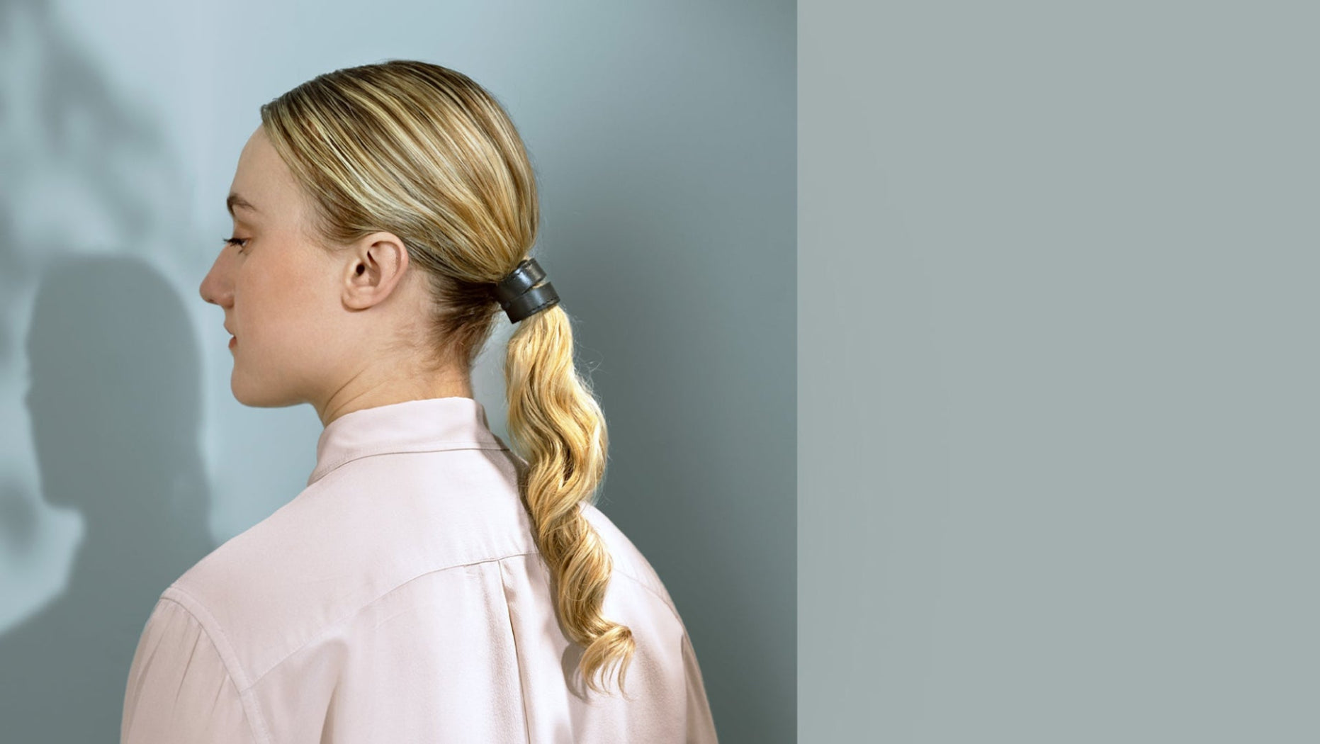 zij aanzicht fashion model met golvend blond haar, haarstyling is een lage staart vastgezet met leren zwarte 2-strap cover in maat S