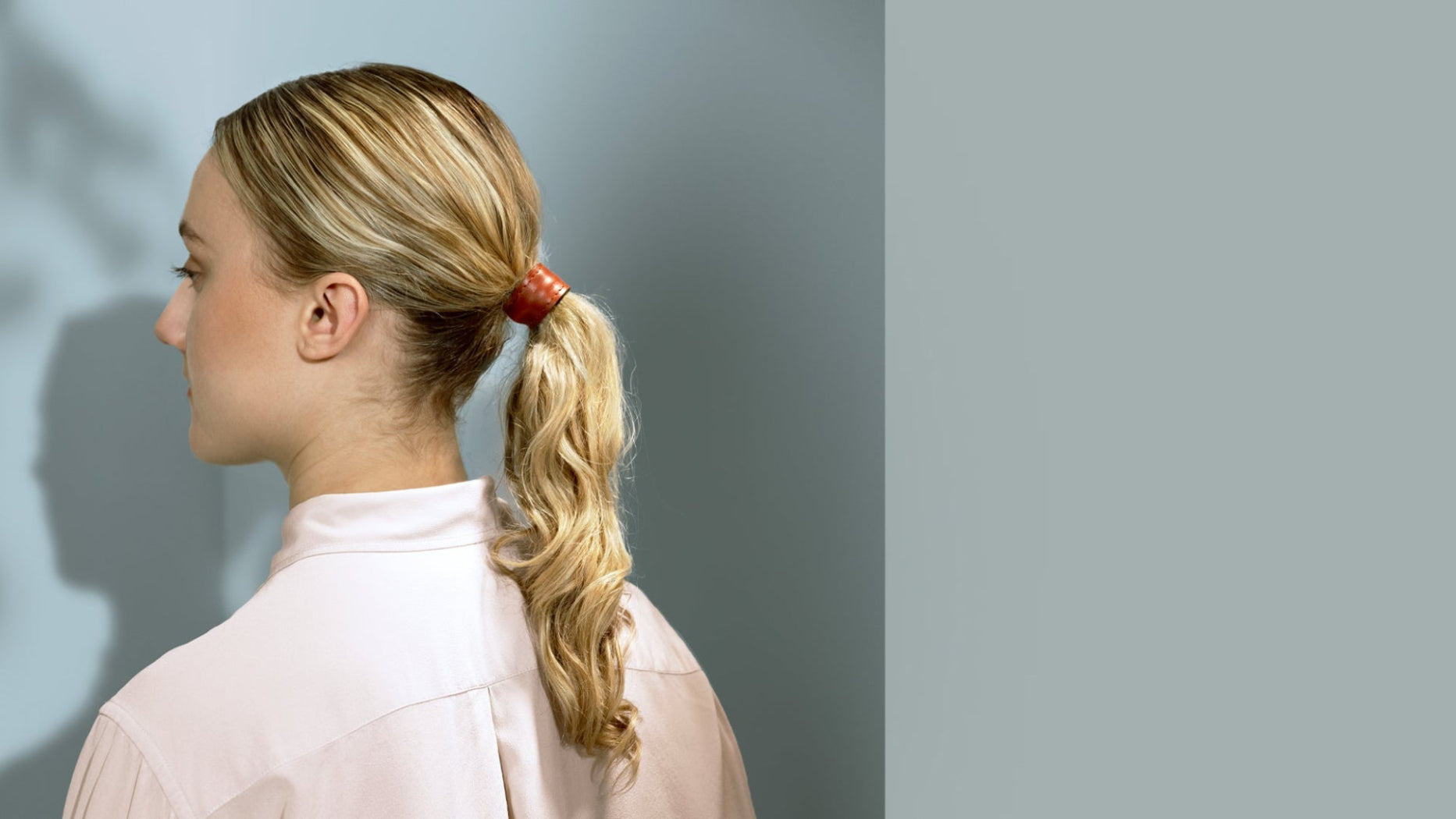 zij aanzicht fashion model met golvend blond haar, haarstyling is paardenstaart met leren haarelatiek in maat M in kleur cognac