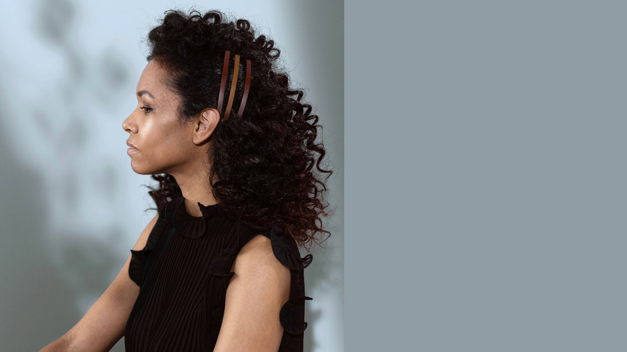fashion model met donker krullend haar, haarstyling is het haar aan de zijkant vastgezet met 3 dunne haarclips in kleuren cognac en sienna bruin