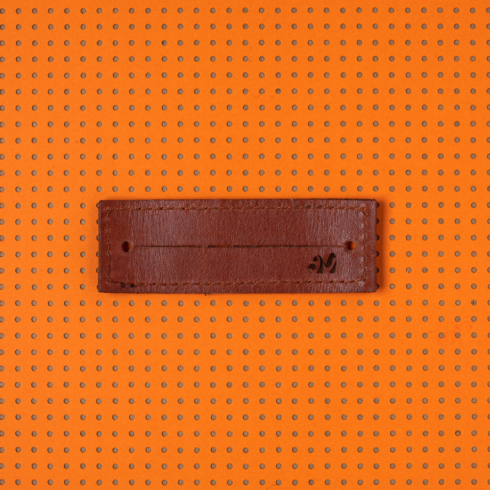 productfoto. 2-strap cover in kleur Sienna bruin plat, binnenzijde product met logo AM rechtsonder. Achtergrond van het beeld is oranje met bruine stippen