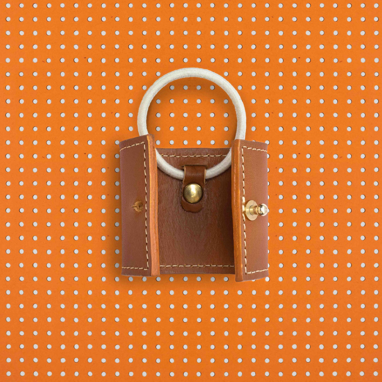 productfoto. Vooraanzicht leren long cover open met elastiek-vervangingssysteem zichtbaar, in kleur cognac met witte stiksels. Achtergrond van het beeld is oranje met bruine stippen