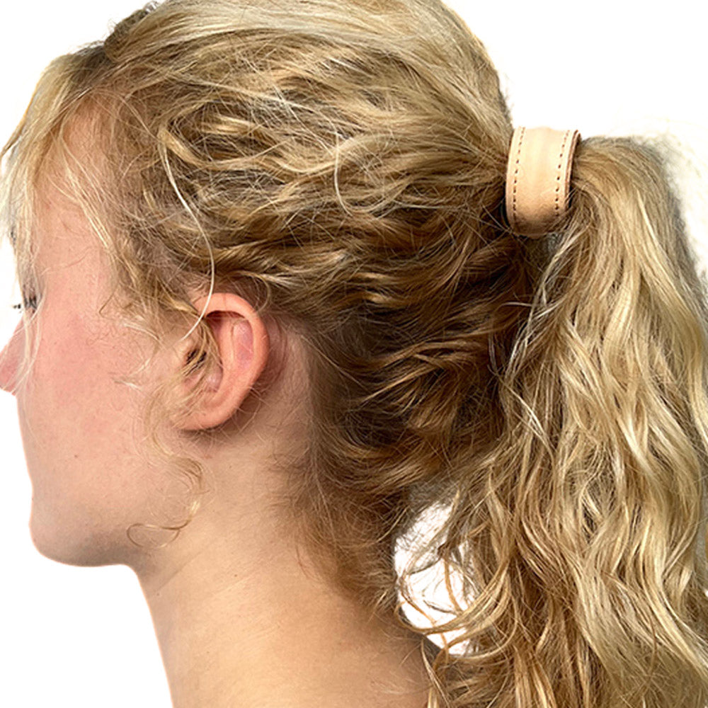 Model met golvend dun blond lang haar, haar in een hoge paardenstaart met een leren haar elastiek in de kleur naturel. Het model draagt een maat S.