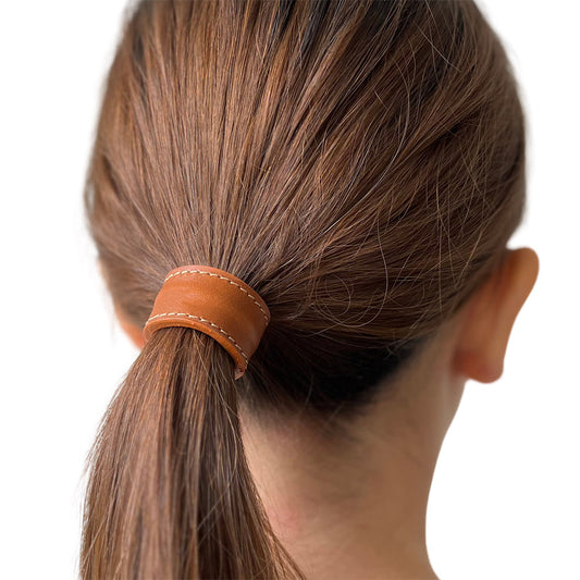 Model met dik bruin stijl lang haar, haar in een lage paardenstaart met short cover in de kleur cognac met witte stiksels. Het model draagt een maat L