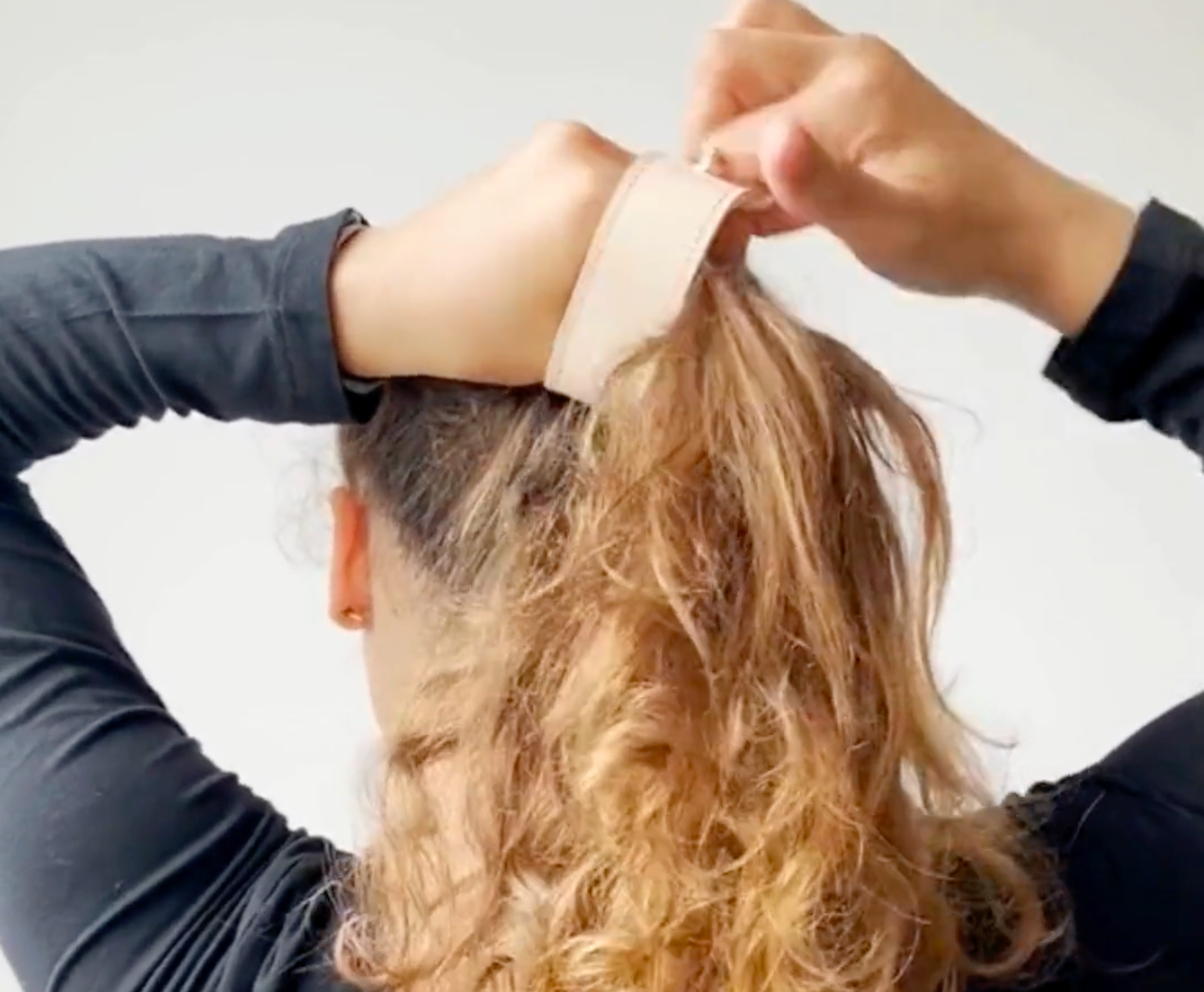 Een still uit de video met een instructie hoe je je short cover leren haaraccessoire gemakkelijk in je staart doet.